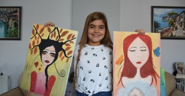 Eight-year-old artist Zeynep Yağmur Çevik poses with two of her paintings in Istanbul, Turkey, Aug. 15, 2022. (AA Photo)