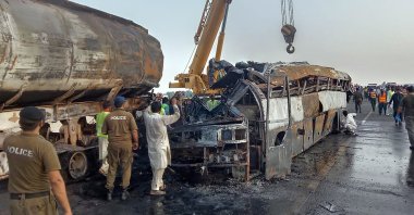 Police officers and workers remove the wreckage of a bus that collided with an oil tanker along a highway in Uch Sharif near Multan, Pakistan, Aug. 16, 2022. (AP Photo)