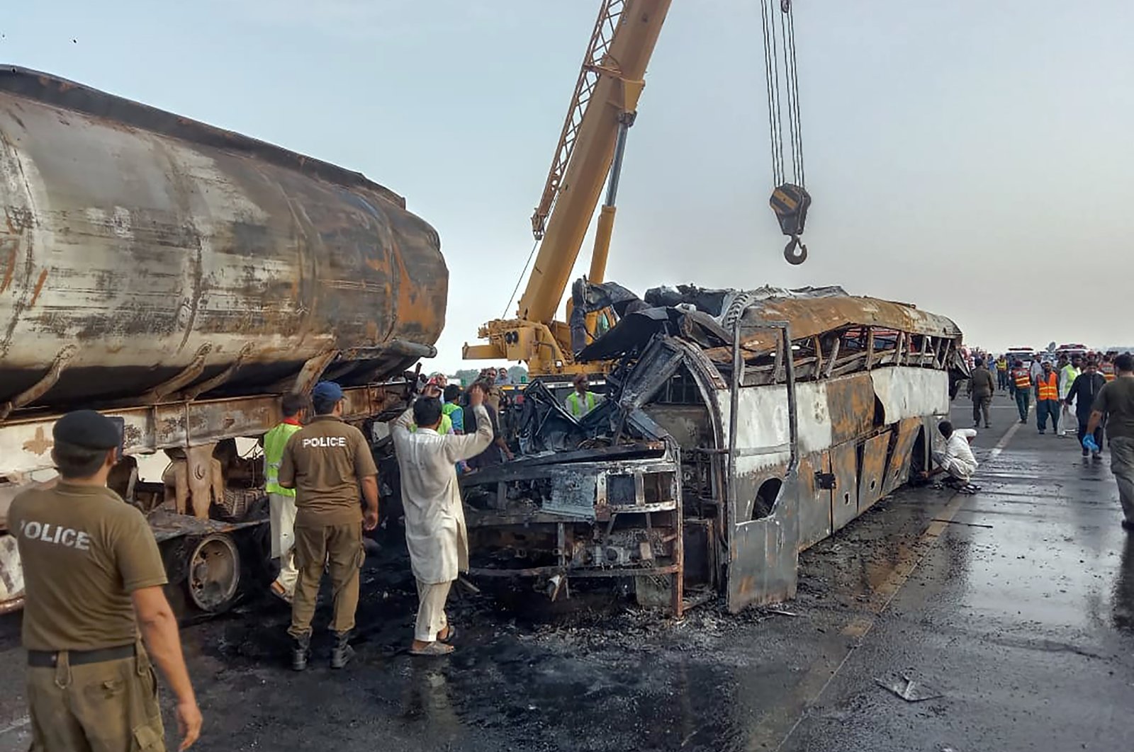 Police officers and workers remove the wreckage of a bus that collided with an oil tanker along a highway in Uch Sharif near Multan, Pakistan, Aug. 16, 2022. (AP Photo)