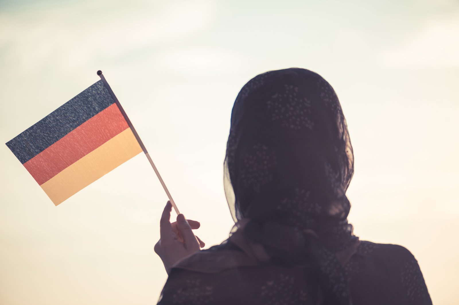 A Muslim woman in a headscarf waves a German flag at sunset. (ShutterStock Photo)