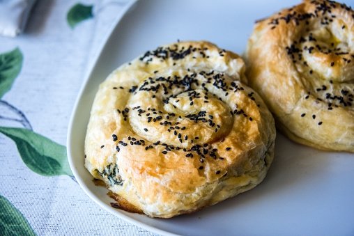A close up shot of homemade cheese and spinach swirl pastries topped with sesame seeds on a plate. (Getty Images)