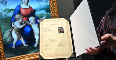 In this file photograph taken on Feb. 15, 2022, a gallery assistant looks at a digital reproduction of the painting &quot;Madonna del Cardellino&quot; (&quot;Madonna of the Goldfinch&quot;) by Raphael, displayed as part of the &quot;Eternalizing Art History: From Da Vinci to Modigliani&quot; exhibition at the Unit London gallery in London, where so-called &quot;NFT&quot; (non-fungible token) digital reproductions of six Italian masterpieces, including paintings by Leonardo da Vinci and Amedeo Modigliani, are on display in London. (AFP Photo)