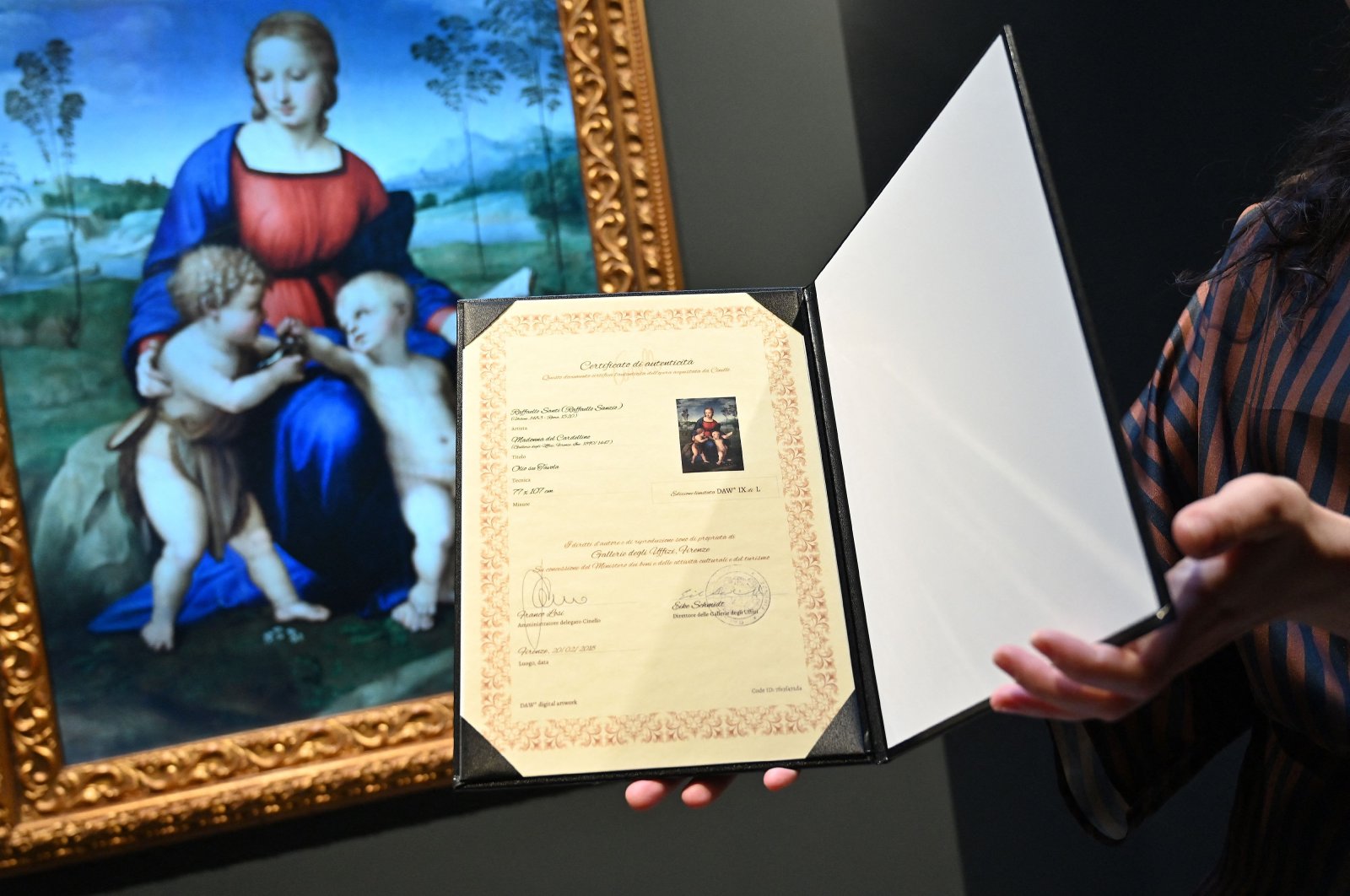 In this file photograph taken on Feb. 15, 2022, a gallery assistant looks at a digital reproduction of the painting &quot;Madonna del Cardellino&quot; (&quot;Madonna of the Goldfinch&quot;) by Raphael, displayed as part of the &quot;Eternalizing Art History: From Da Vinci to Modigliani&quot; exhibition at the Unit London gallery in London, where so-called &quot;NFT&quot; (non-fungible token) digital reproductions of six Italian masterpieces, including paintings by Leonardo da Vinci and Amedeo Modigliani, are on display in London. (AFP Photo)