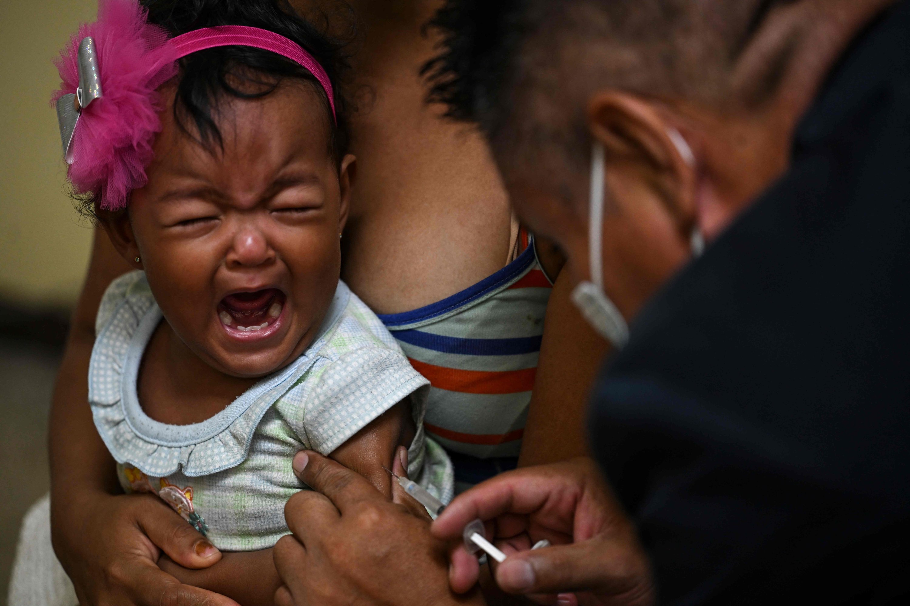 Seorang gadis yang ditemani ibunya menerima satu dosis vaksin campak dan rubella dari petugas medis di sebuah pusat kesehatan masyarakat di lingkungan Lidice di Caracas, Venezuela, 17 Agustus 2022. (AFP Photo)