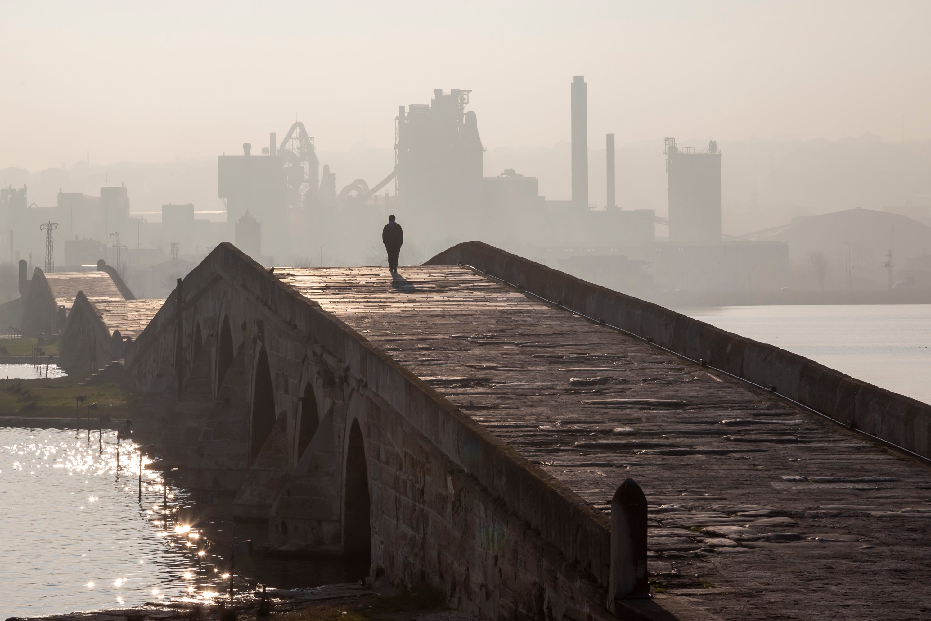 Siluet pria paruh baya berjalan di Suleiman the Magnificent Bridge, di depan latar belakang pabrik industri yang berkabut, Istanbul, Türkiye.  (Foto Shutterstock)