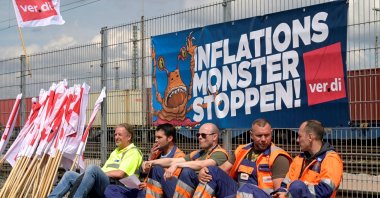Workers sit in front of a banner reading "Stop the Inflation Monster" at the Burchardkai Container Terminal as they go on strike for higher wages in the harbor in Hamburg, Germany, June 9, 2022. (Reuters Photo)