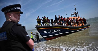 A British police officer stands guard on the beach of Dungeness, on the southeast coast of England, as Royal National Lifeboat Institution's (RNLI) members help migrants to disembark from one of their lifeboats after they were picked up at sea while attempting to cross the English Channel, June 15, 2022. (AFP Photo)