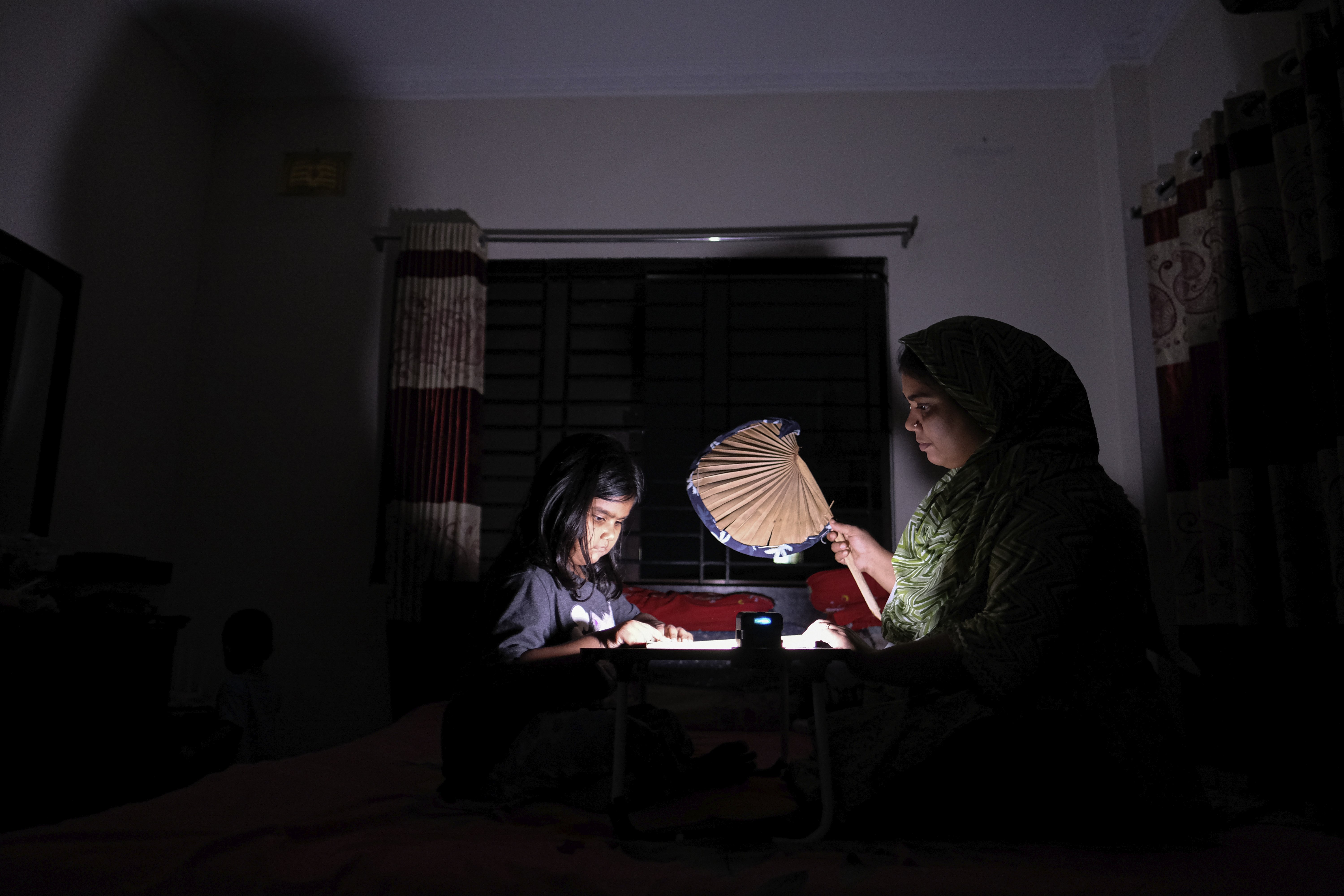 A Bangladeshi woman uses a traditional hand fan as she assists her daughter in her studies during a power cut at their home in Pilkhana area, Dhaka, Bangladesh, Aug. 23, 2022. (AP Photo/Mahmud Hossain Opu)