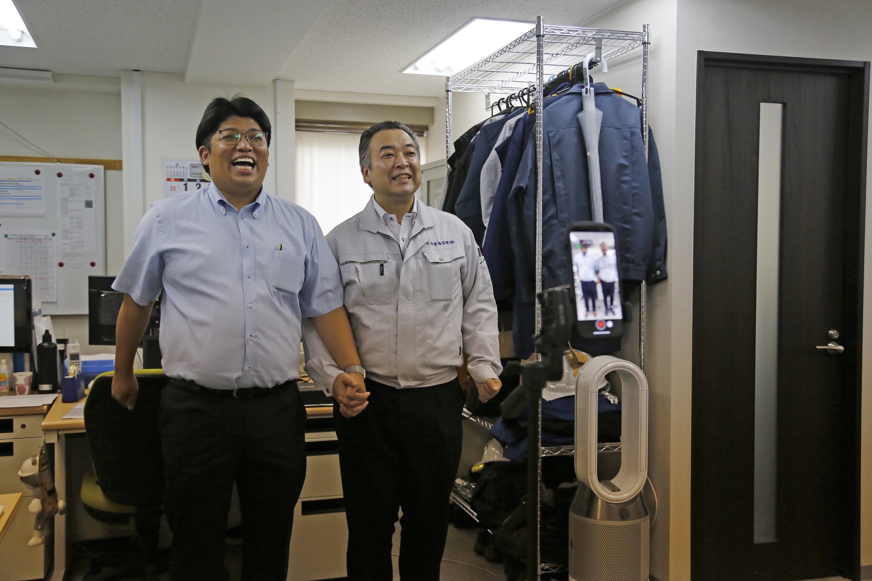 Kepala Eksekutif Keamanan Daikyo Daisuke Sakurai (kiri) dan Manajer Umum Tomohiko Kojima mengambil video Tik Tok bersama-sama seperti yang terlihat di layar perangkat (kanan) di kantor pusat Daikyo Security Co. Tokyo, Jepang, 22 Agustus 2022 (Foto AP)