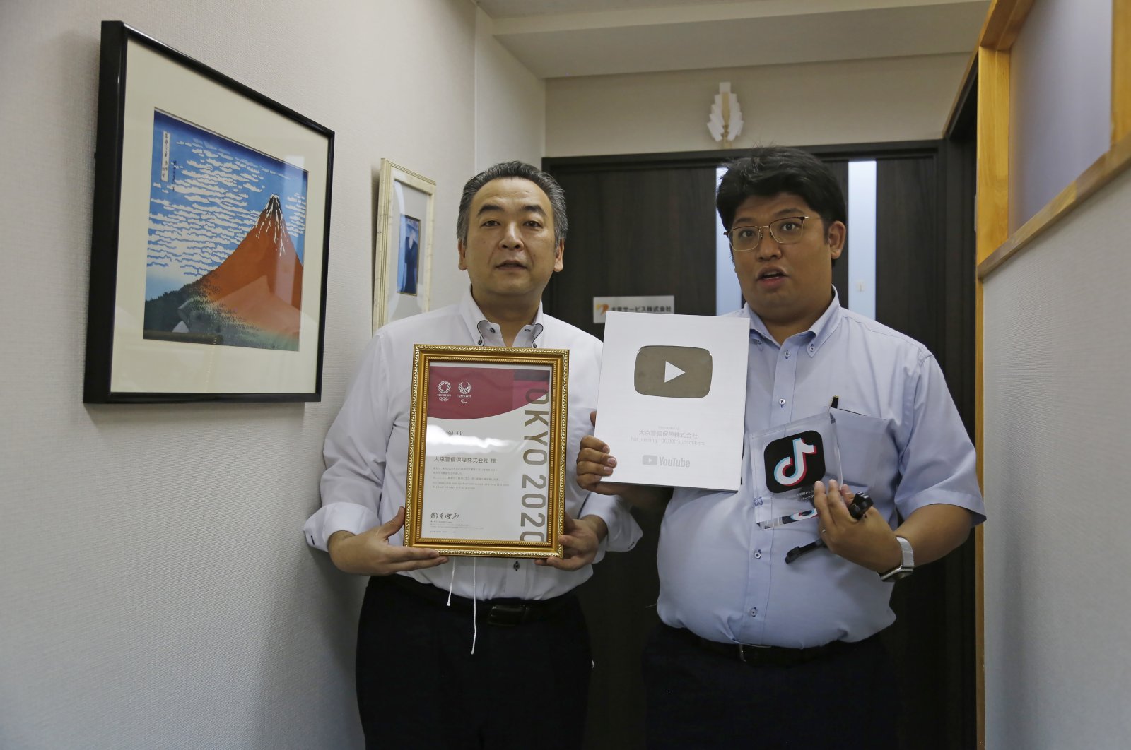 Daikyo Security Chief Executive Daisuke Sakurai (R), and General Manager Tomohiko Kojima hold the awards they have won recently for their Tik Tok videos in the hallway of their Tokyo headquarters office of Daikyo Security Co. Tokyo, Japan, Aug. 22, 2022. (AP Photo)