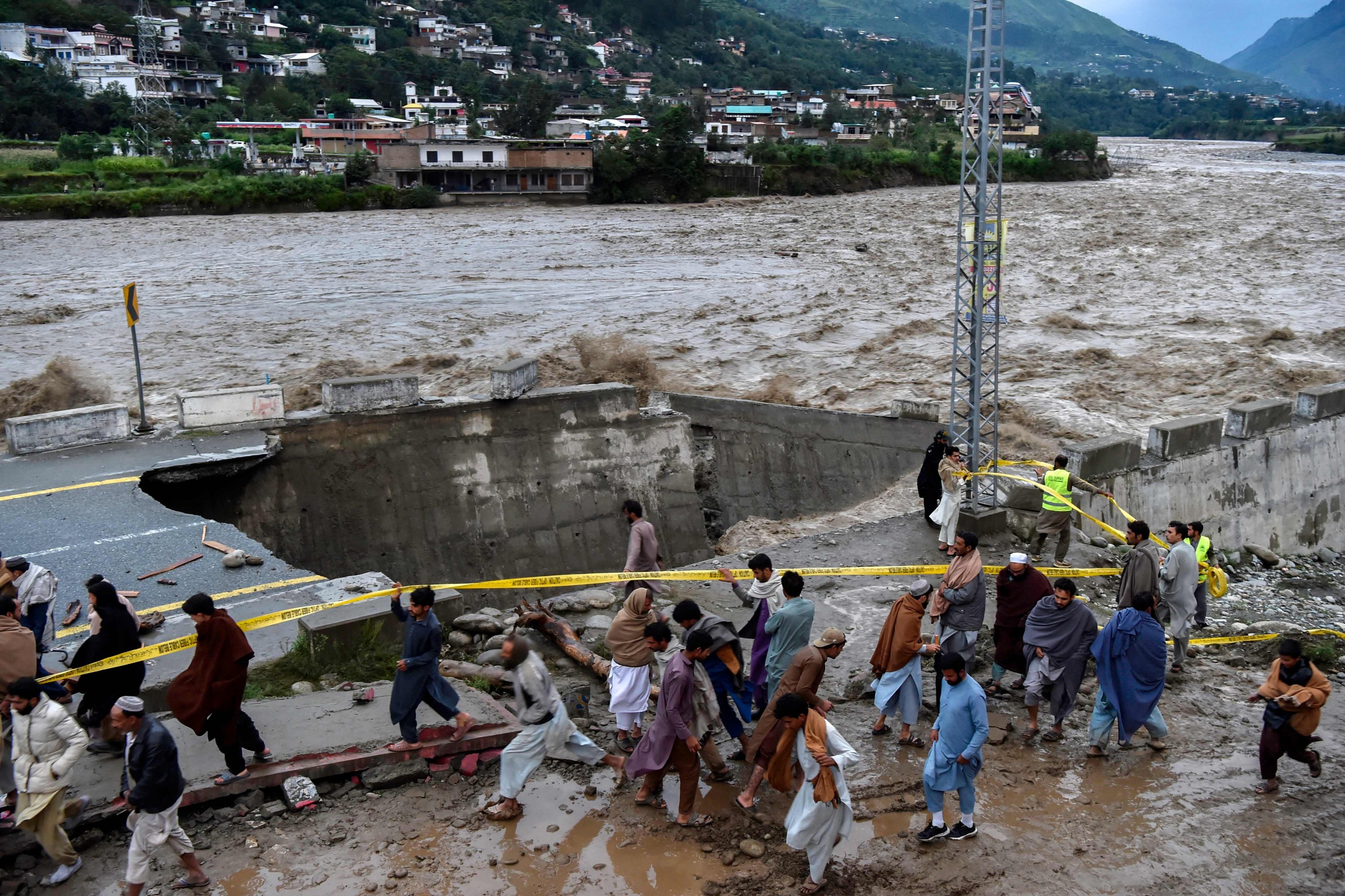 Orang-orang berkumpul di depan jalan yang rusak akibat banjir, Madian, Pakistan utara, 27 Agustus 2022. (AFP Photo)
