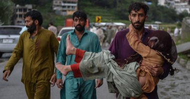 A man (R) carries his sick daughter along a road damaged by flood waters following heavy monsoon rains, Madian, northern Pakistan, Aug. 27, 2022. (AFP Photo)