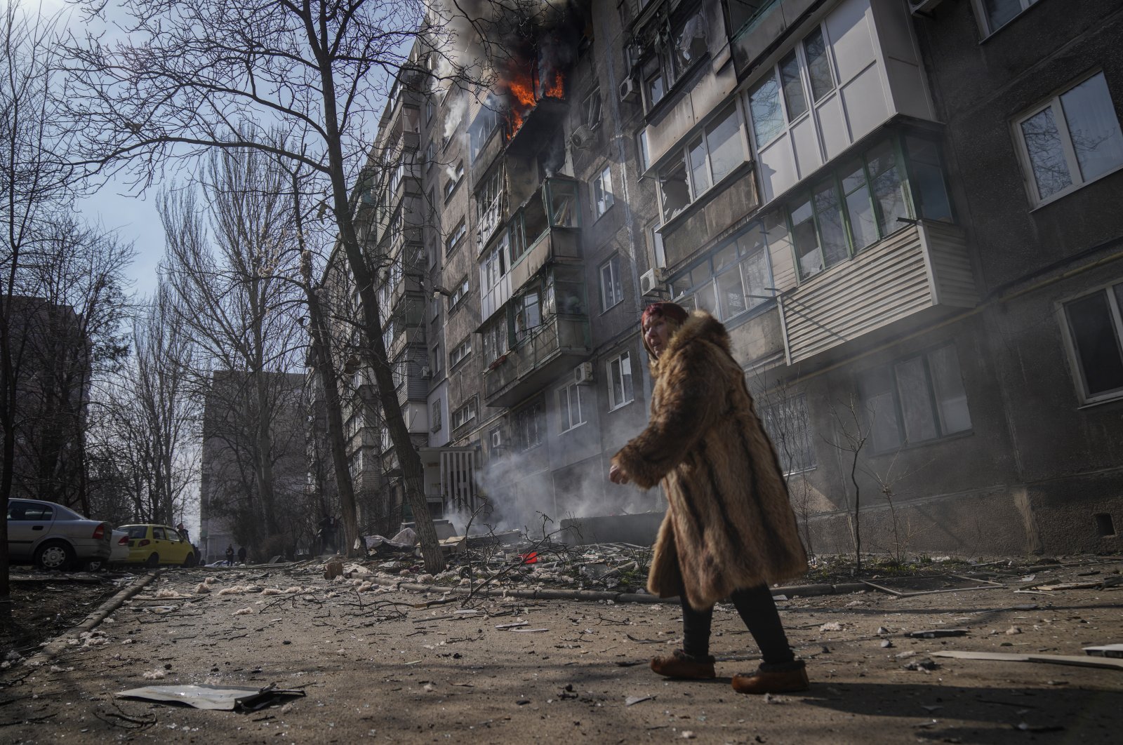 A woman walks past a burning apartment building after shelling in Mariupol, Ukraine, March 13, 2022. (AP Photo)