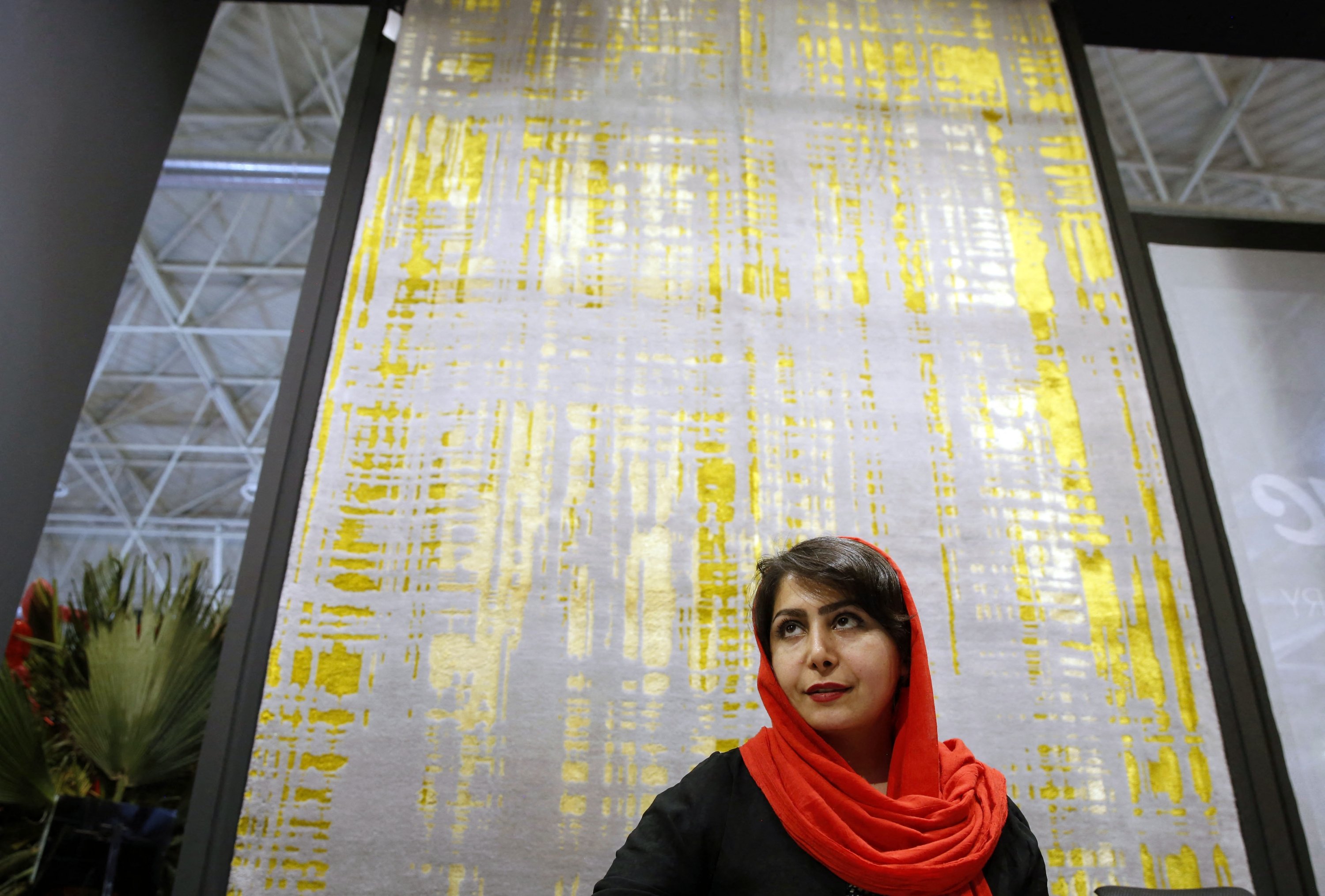 Seorang anggota staf berdiri di samping karpet wol abu-abu Isfahan dengan motif sutra kuning dan hijau di Pameran Karpet Buatan Tangan ke-29 di ibukota Iran, Teheran, 26 Agustus 2022. (AFP)