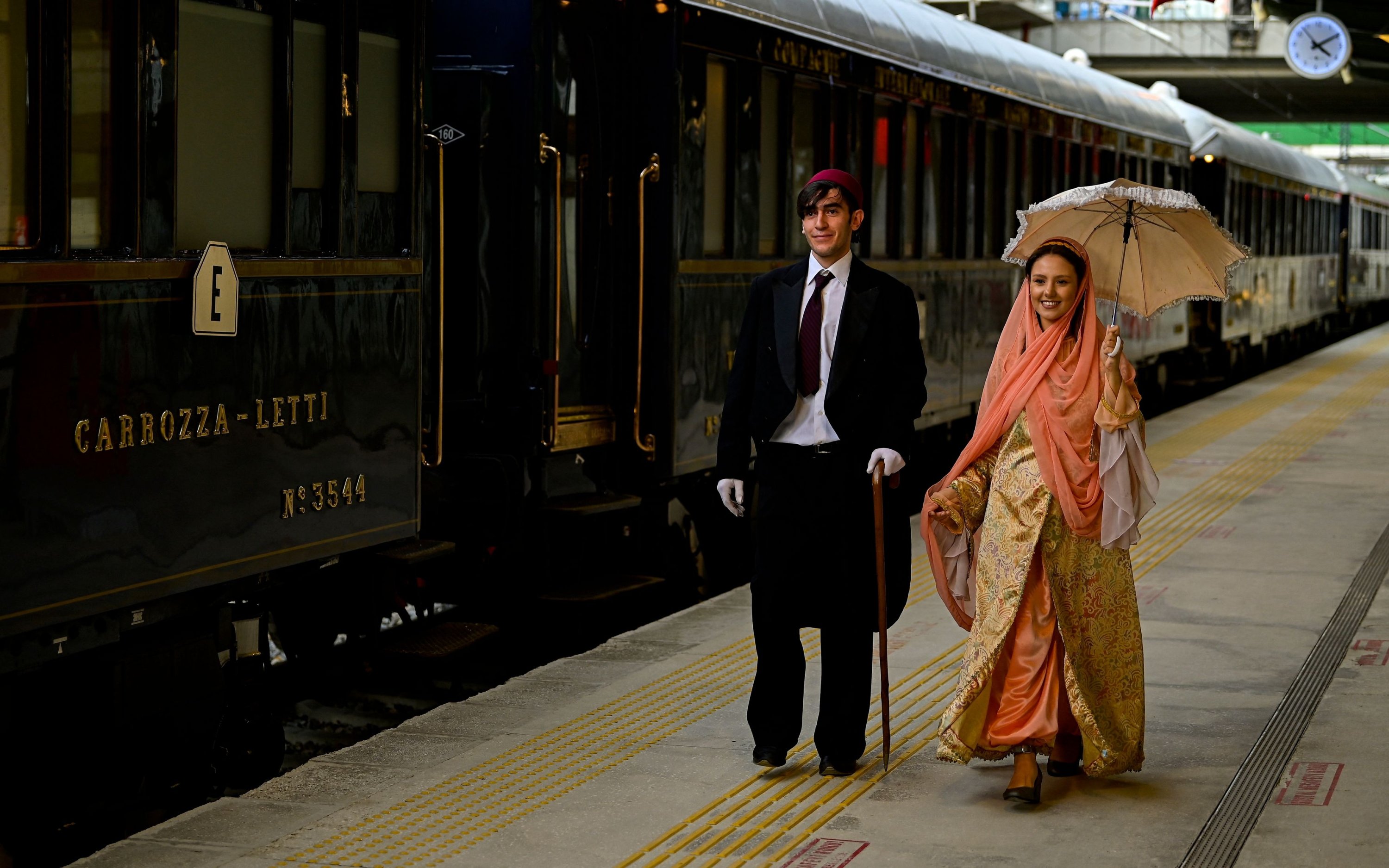 Dua orang mengenakan kostum era Ottoman berjalan melewati Venice Simplon-Orient-Express saat upacara penyambutan di Stasiun Istanbul, Türkiye, 31 Agustus 2022. (AFP Photo)