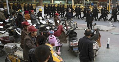 Residents watch a convoy of security personnel armed with batons and shields patrol through central Kashgar in Xinjiang region, China, Nov. 5, 2017. (AP Photo)