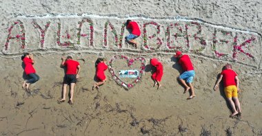 Activists lie on the beach next to flowers reading "Aylan Baby" in Turkish, where Kurdi died, in Muğla, southwestern Türkiye, Sept. 2, 2022. (AA PHOTO)