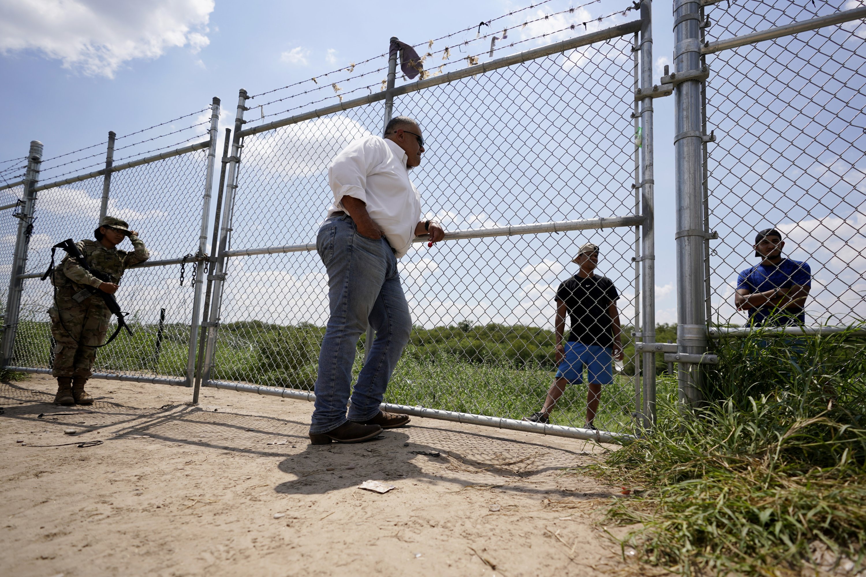 Hugo Urbina (tengah) berbicara melalui pagarnya kepada para migran yang menyeberangi Rio Grande secara ilegal di peternakan pecan miliknya, Texas, AS, 26 Agustus 2022. (AP Photo)