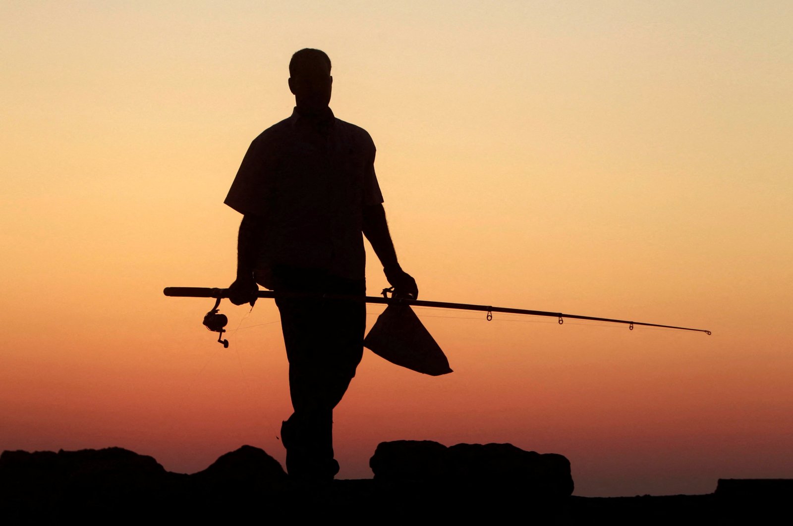 A man carries a fishing rod during sunset along the shoreline in the Mediterranean city of Alexandria, 230 kilometers (140 miles) north of Cairo, Egypt, July 12, 2011. (Reuters File Photo)
