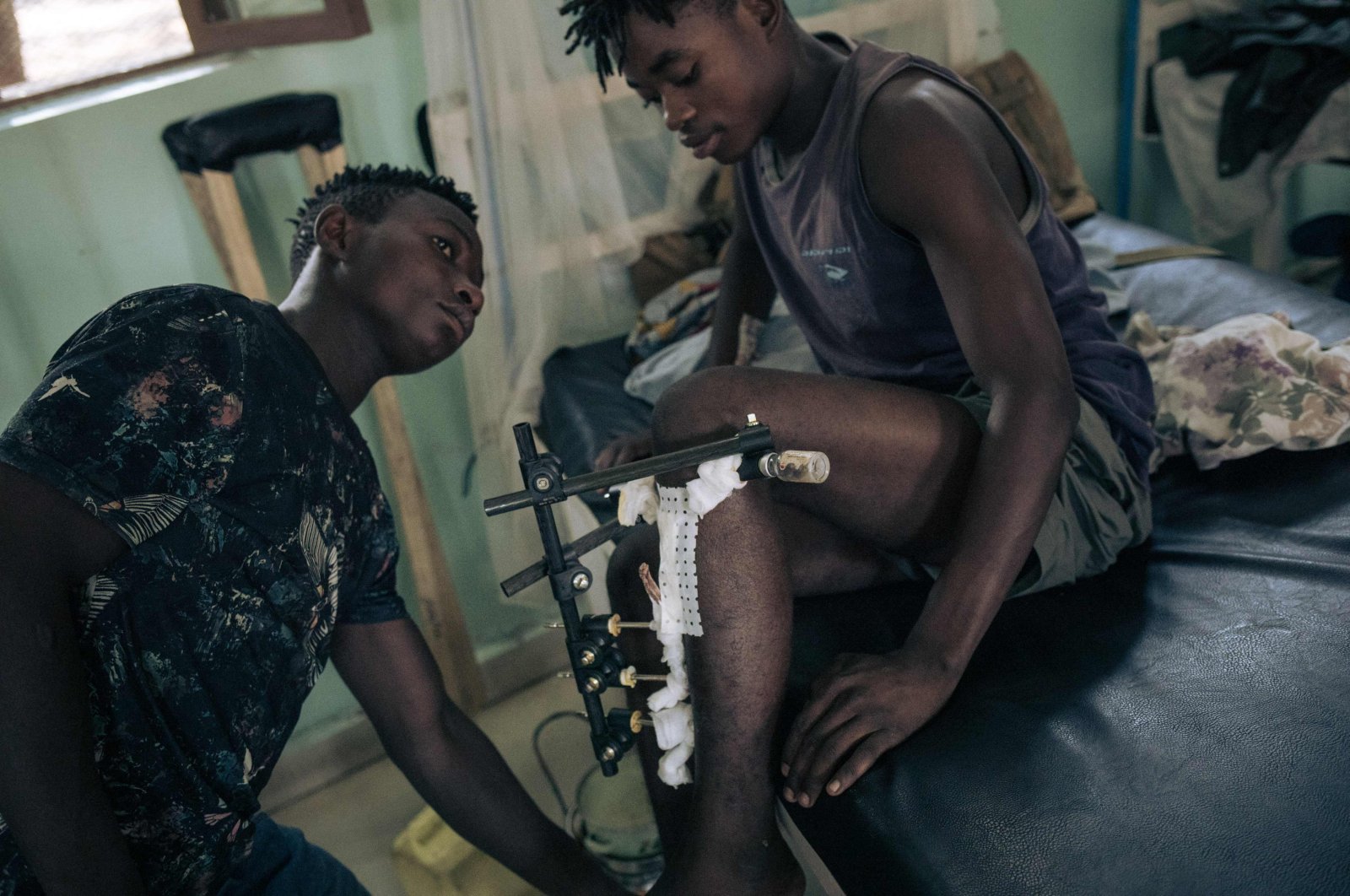 A young man with a gunshot wound on the leg with his attendant at Rutshuru Hospital in the eastern province of North Kivu, Democratic Republic of Congo, July 23, 2022. (Photo by ALEXIS HUGUET / AFP)