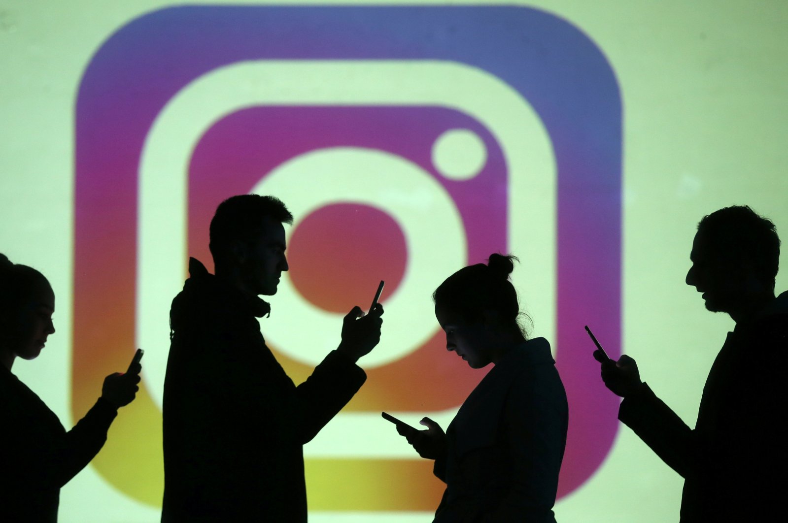 Silhouettes of mobile users are seen next to a screen projection of the Instagram logo in this picture illustration taken March 28, 2018. (Reuters Photo)