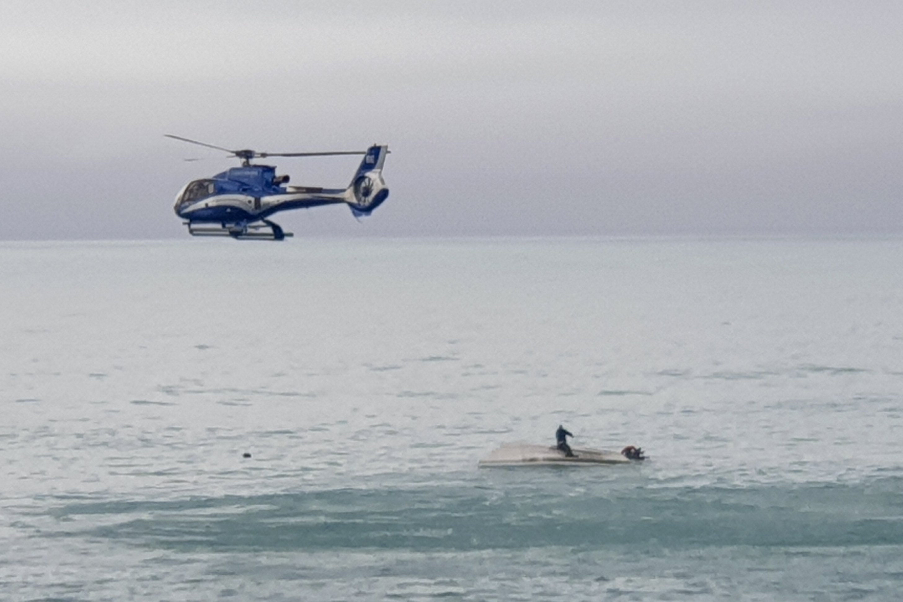 A helicopter flies over an upturned boat with a survivor sitting on the hull off the coast of Kaikoura, New Zealand, Sept. 10, 2022. (AP Photo)