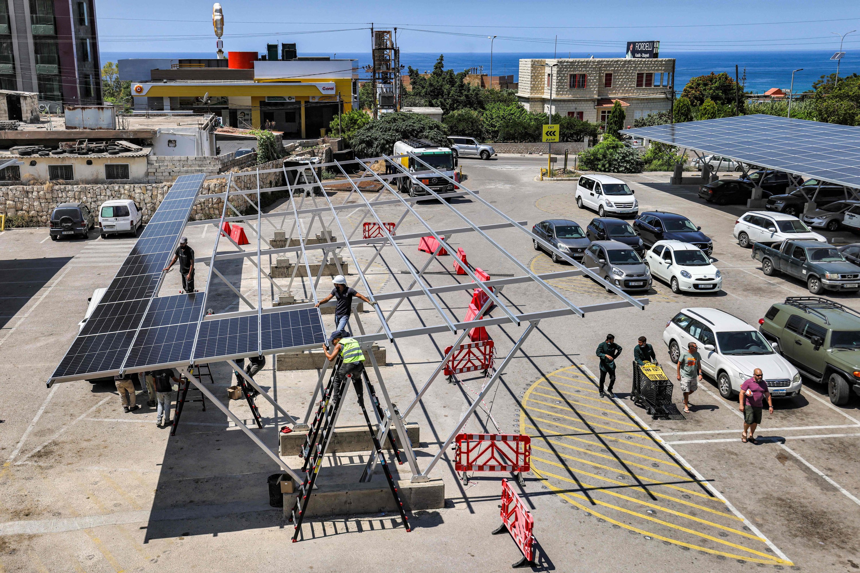 Trabalhadores instalam painéis solares no estacionamento de um shopping na cidade de Byblos, norte do Líbano, 26 de agosto de 2022 (Foto AFP)