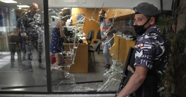 A Lebanese policeman stands guard next to a bank window that was broken by depositors to exit the bank after attacking it trying to get their money, in Beirut, Lebanon, Sept. 14, 2022. (AP Photo)