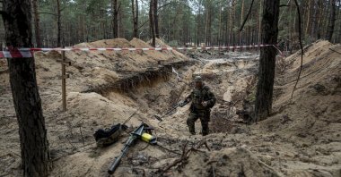 A Ukrainian soldier uses a metal detector to inspect a mass grave in the recently retaken area of Izium, Ukraine, Sept. 15, 2022. (AP Photo)