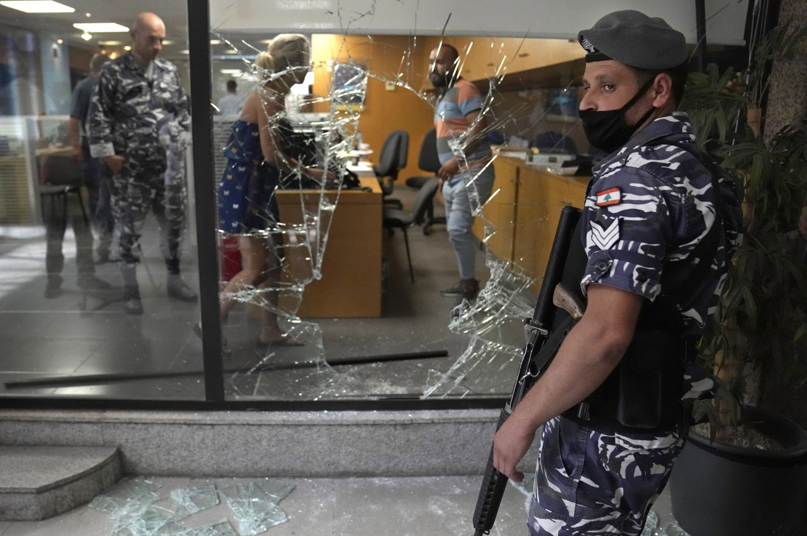 A Lebanese policeman stands guard next to a bank window that was broken by depositors to exit the bank after attacking it trying to get their money, in Beirut, Lebanon, Sept. 14, 2022. (AP Photo)