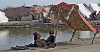 Flood victims sit under the shadow of a cot on a roadside, Jaffarabad, Pakistan, Sept. 19, 2022. (AP Photo)