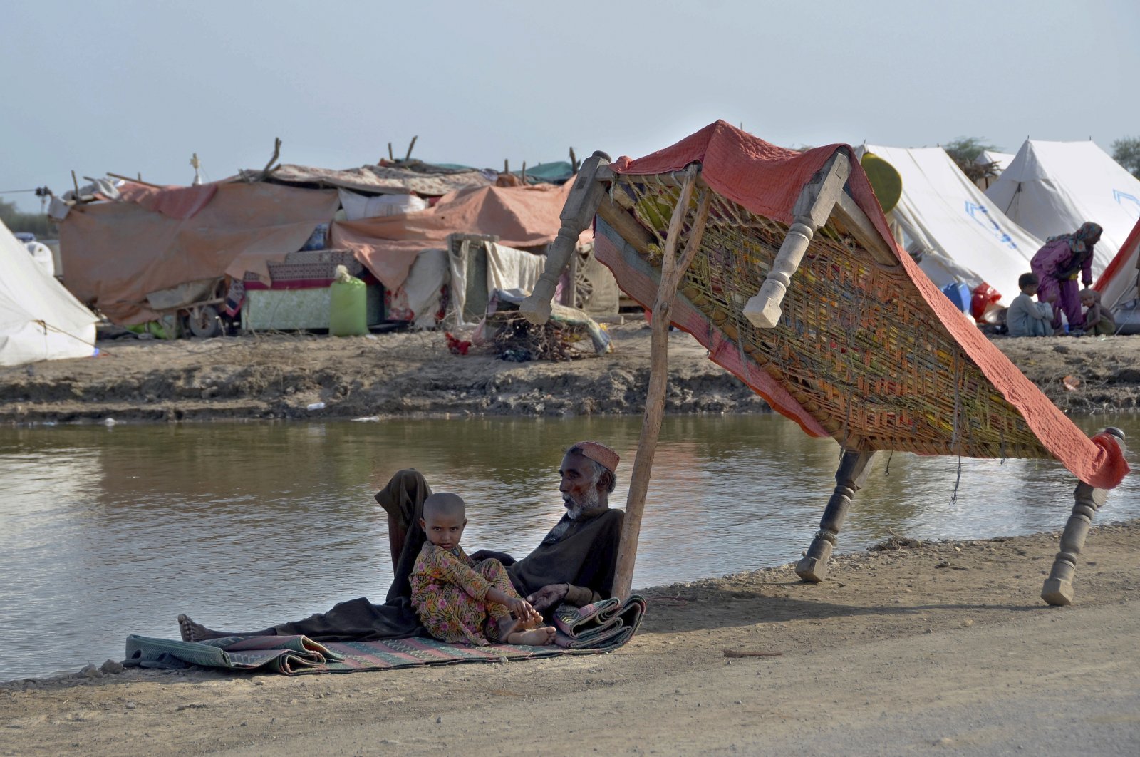 Flood victims sit under the shadow of a cot on a roadside, Jaffarabad, Pakistan, Sept. 19, 2022. (AP Photo)