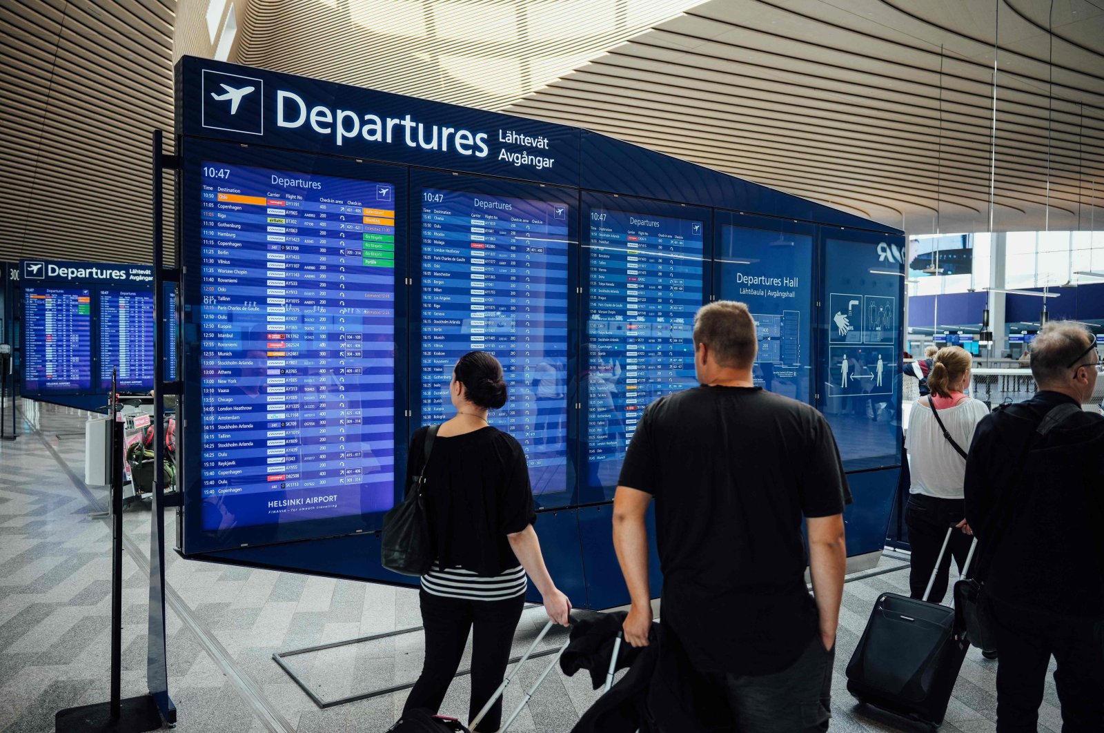 Travelers stand in front of a departures board inside  Terminal 2 of Helsinki Airport, Vantaa, Finland, Aug. 19, 2022. (AFP Photo)
