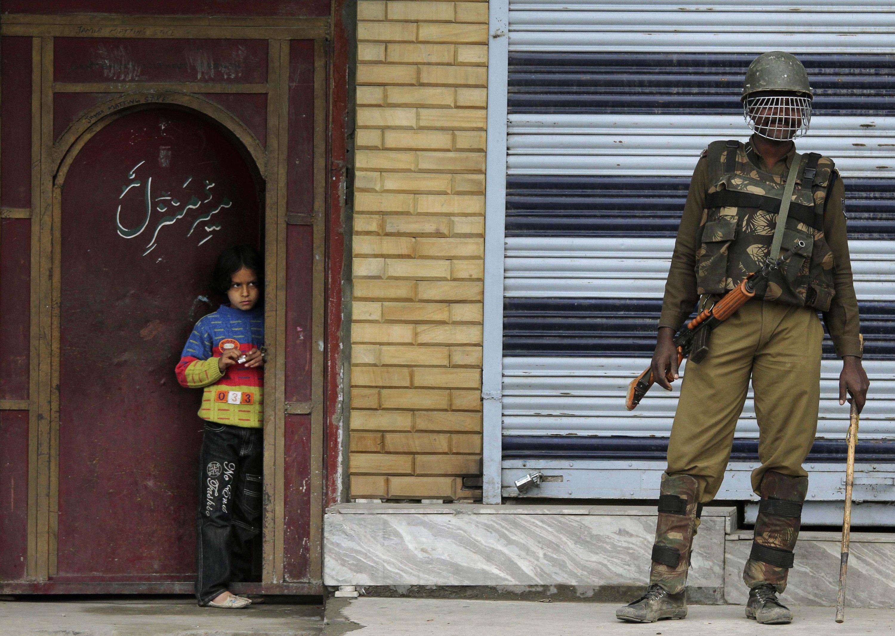 Seorang tentara paramiliter India berjaga-jaga saat seorang gadis Kashmir mengawasi dari ambang pintu selama pemogokan di Srinagar, Kashmir yang dikelola India, 23 April 2010. (AP Photo)