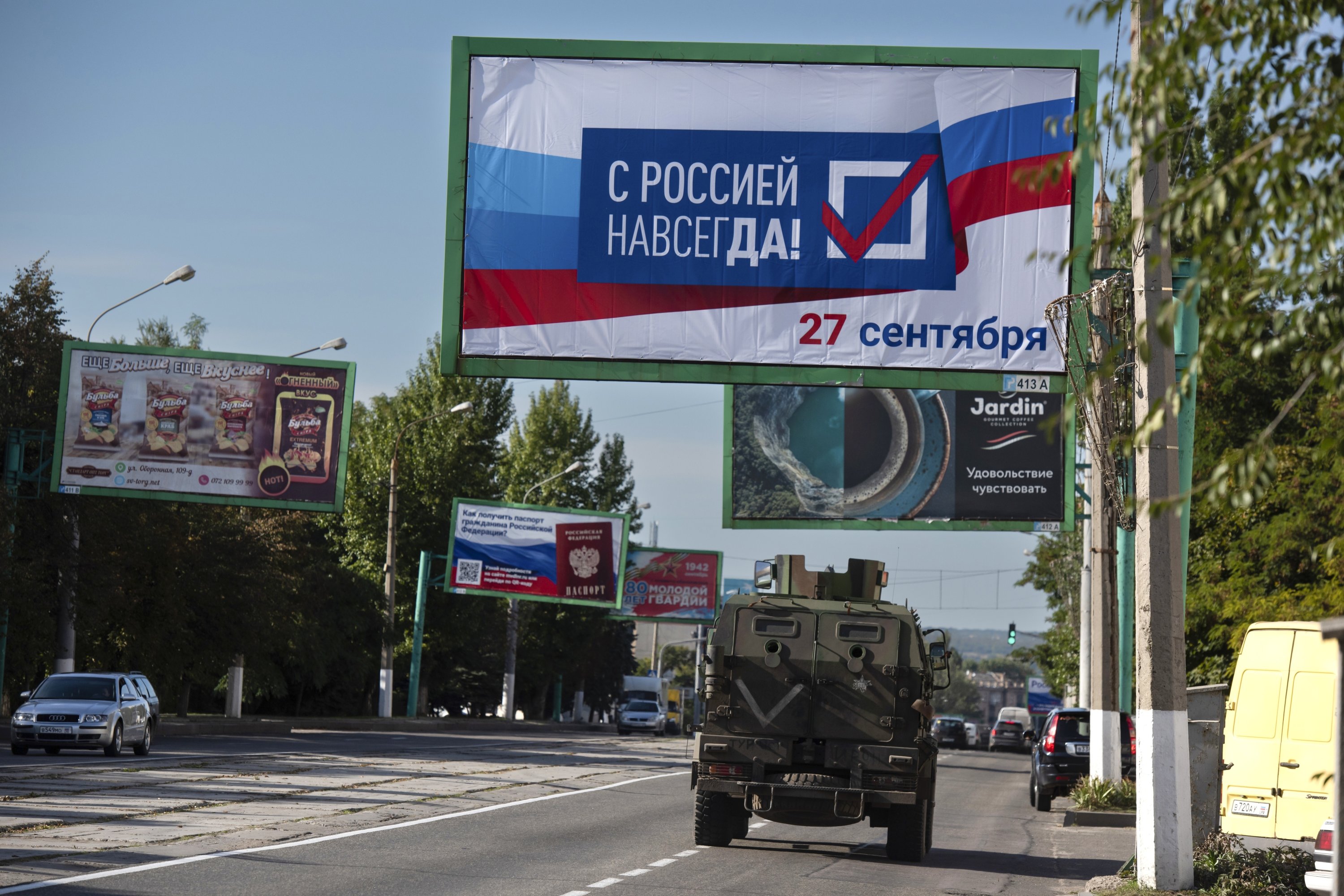 Sebuah kendaraan militer melaju di sepanjang jalan dengan papan reklame yang berbunyi: 
