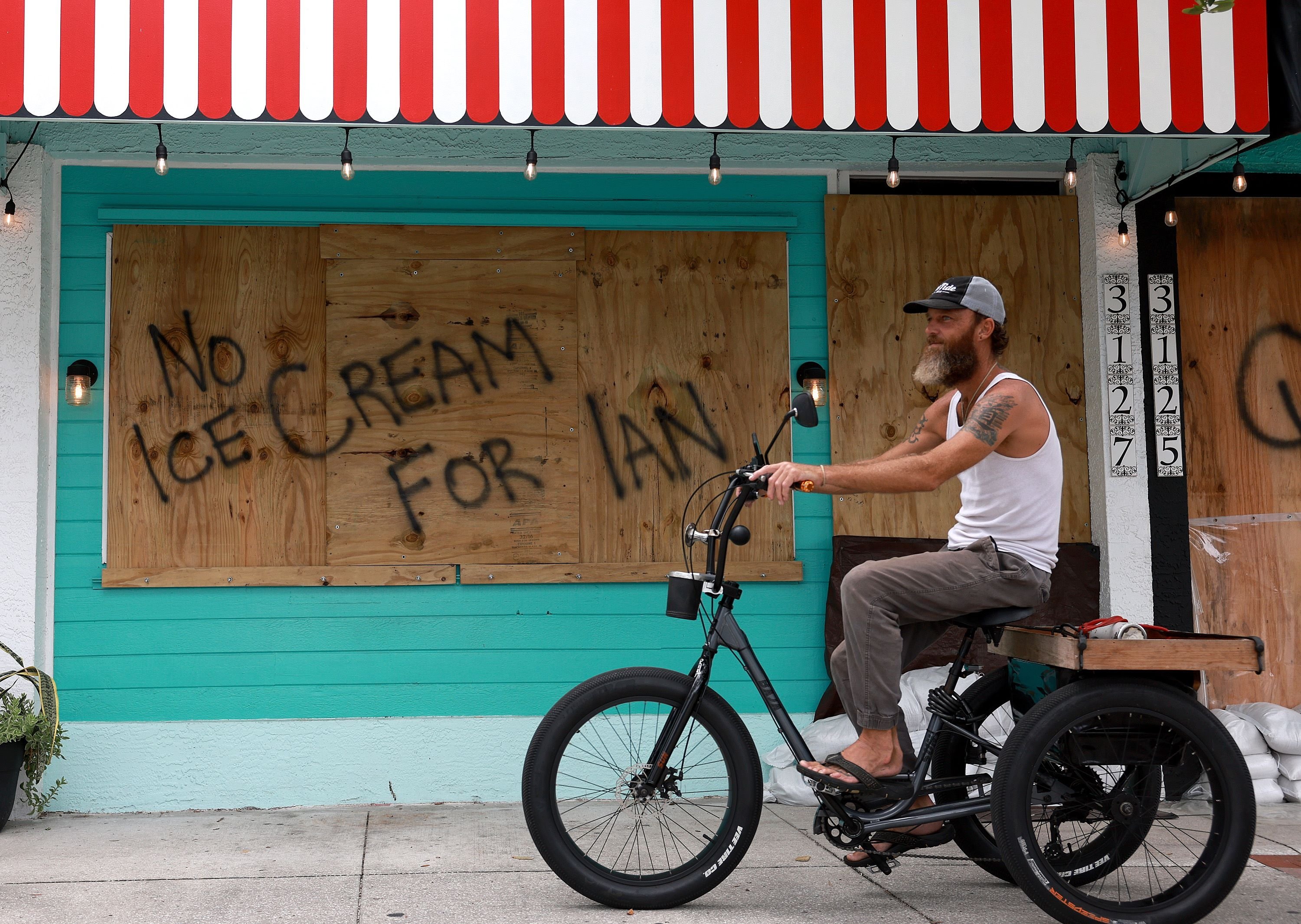 A bicyclist rides past a sign reading, 'No Ice Cream for Ian,' painted on a boarded-up building, St. Petersburg, Florida, U.S., Sept. 27, 2022. (AFP Photo)