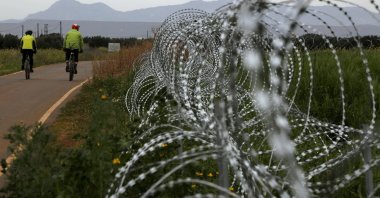 Two men cycle along a row of razor wire along the southern side of a U.N buffer zone that cuts across the ethnically divided Cyprus, March 9, 2021. (AP Photo)