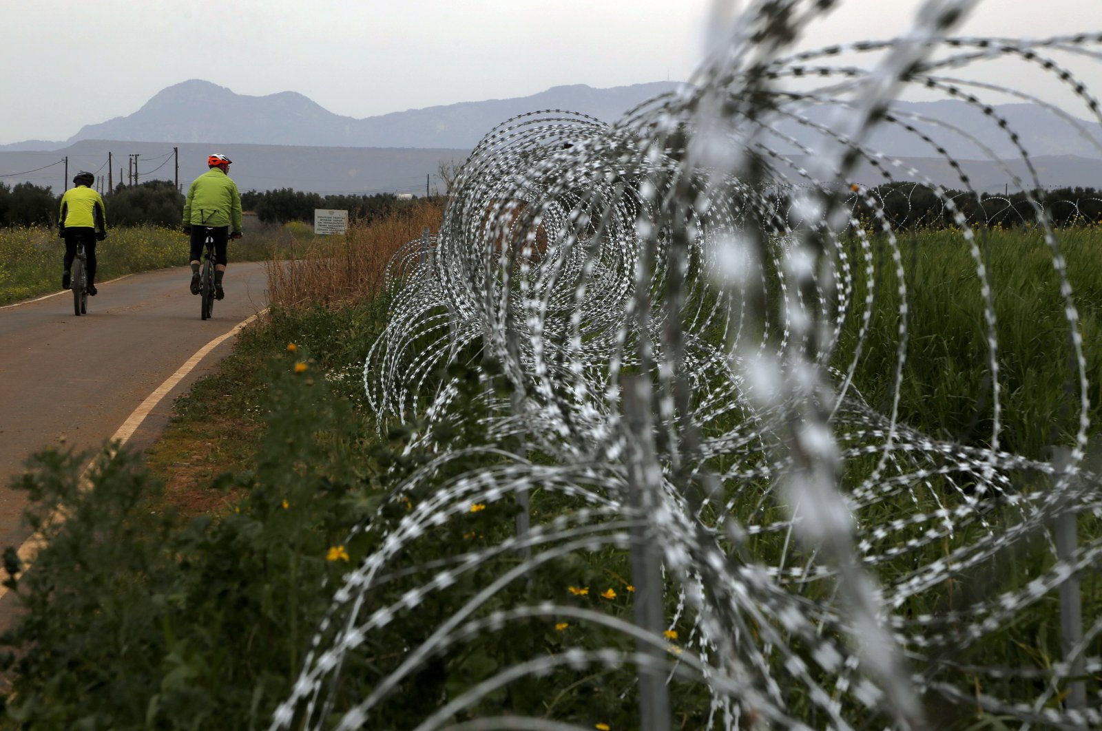 Two men cycle along a row of razor wire along the southern side of a U.N buffer zone that cuts across the ethnically divided Cyprus, March 9, 2021. (AP Photo)