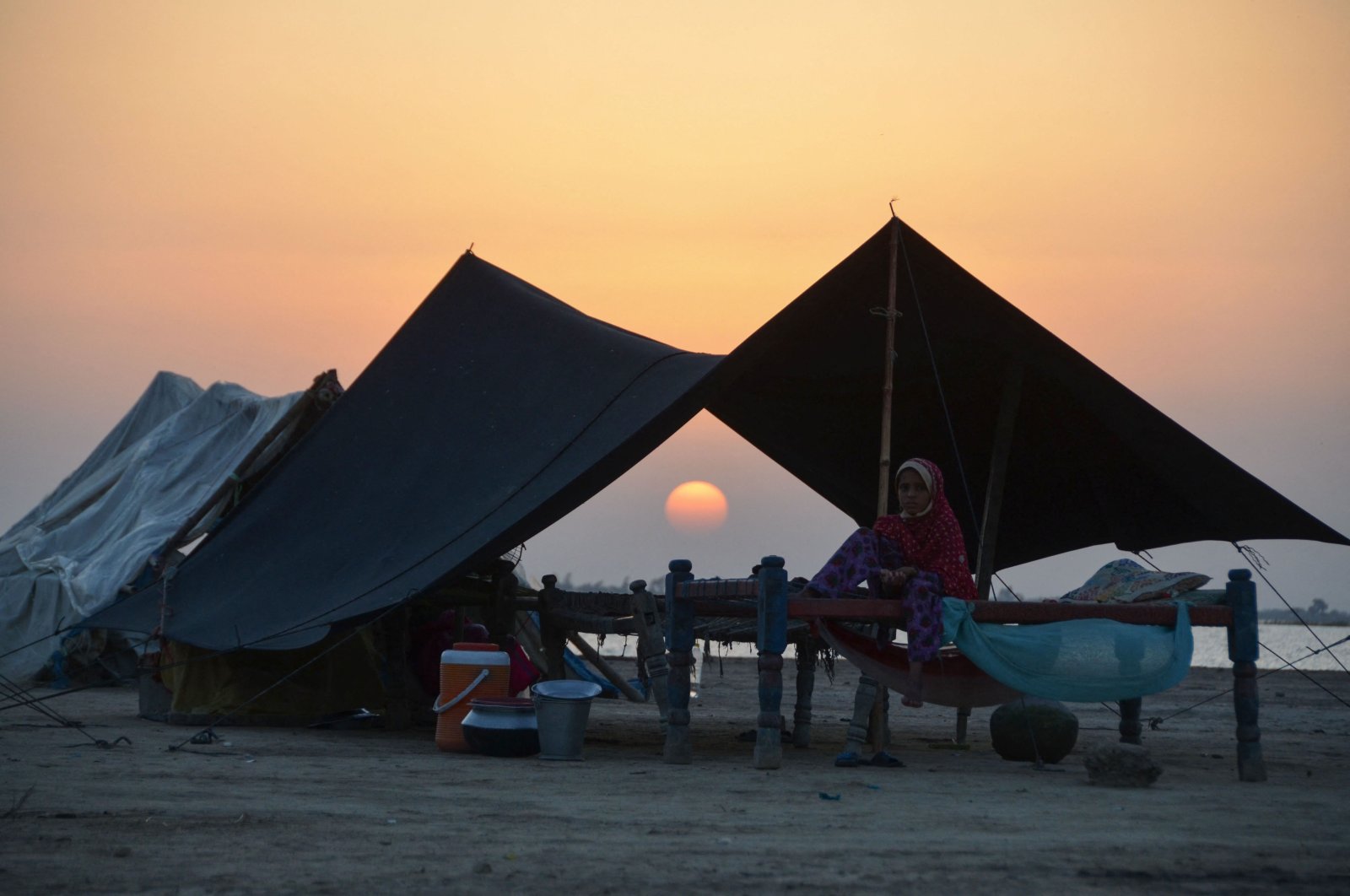An internally displaced flood-affected girl sits in her tent at sunset at a camp in the flood-hit area in Dera Allah Yar in Jaffarabad district of Balochistan province, Pakistan, Sept. 28, 2022. (AFP Photo)