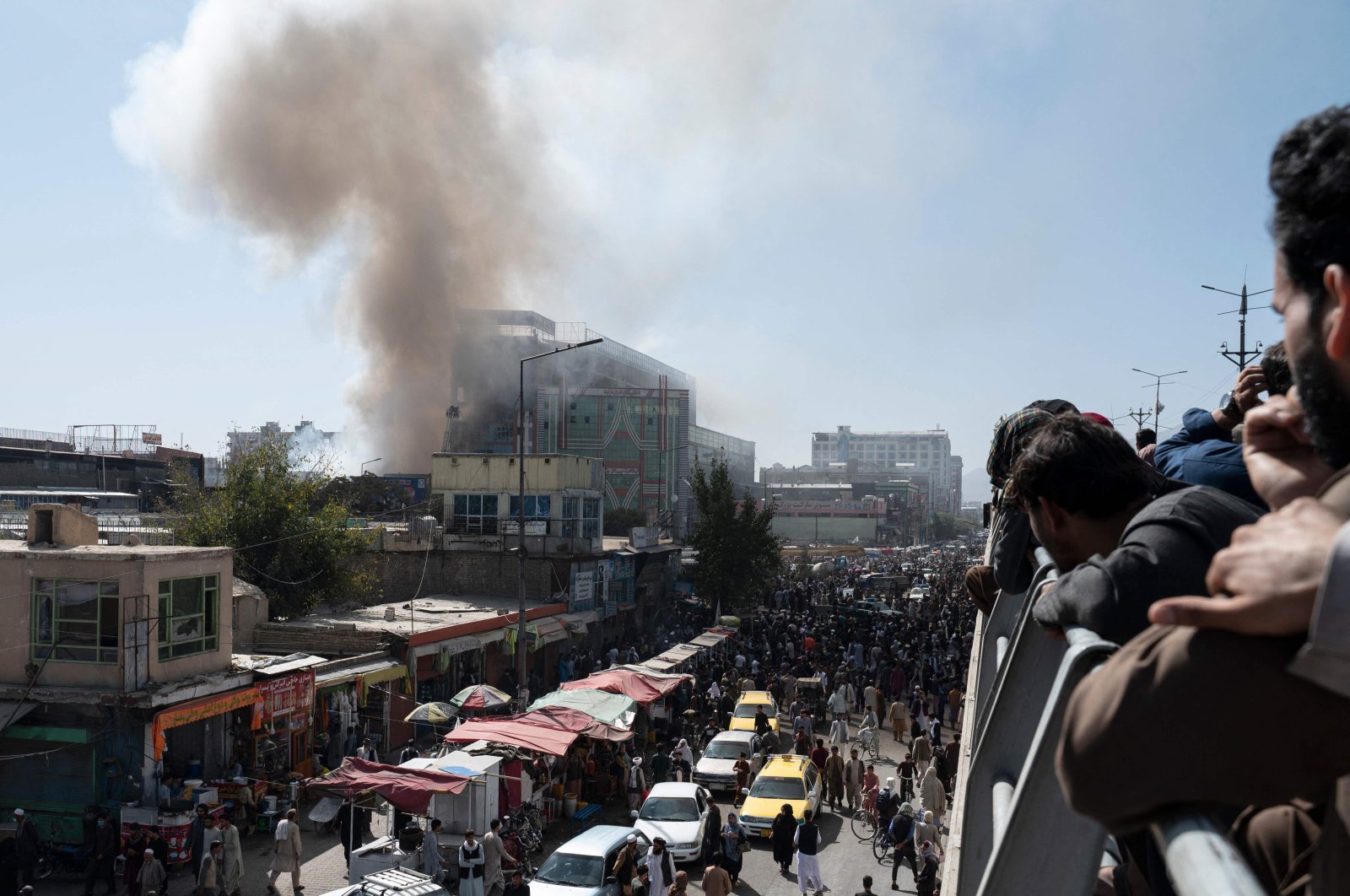 People watch smoke billowing from a fire at a business center mall in Kabul, Afghanistan, Oct. 5, 2022. (Photo by Wakil KOHSAR / AFP)