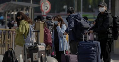 Travelers wearing face masks wait for their transport near a train station, Beijing, China, Oct. 6, 2022. (AP Photo)