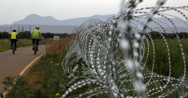 Two men cycle along a row of razor wire along the southern side of a U.N buffer zone that cuts across the ethnically divided island of Cyprus, March 9, 2021. (AP Photo)