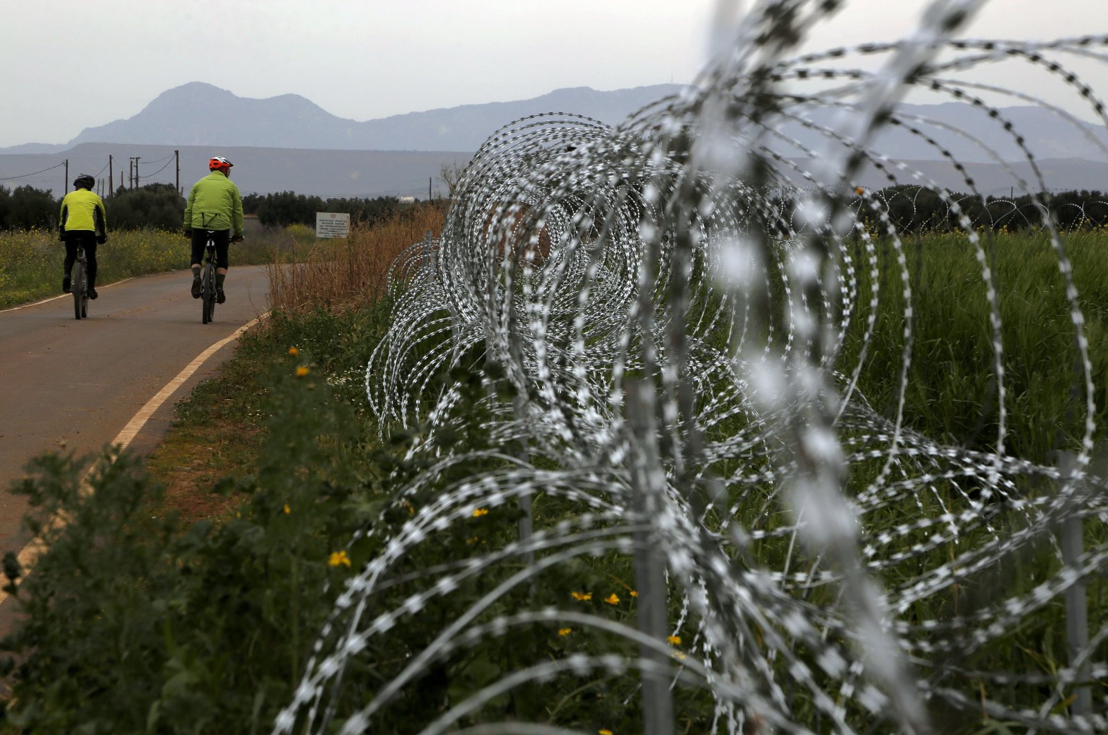 Two men cycle along a row of razor wire along the southern side of a U.N buffer zone that cuts across the ethnically divided island of Cyprus, March 9, 2021. (AP Photo)