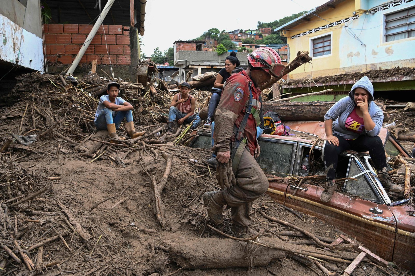 Residents remain on top of a semi-buried vehicle as rescuers search for their missing relatives after a landslide washed away dozens of homes during heavy rains, Las Tejerias, Aragua state, Venezuela, Oct. 9, 2022. (AFP Photo)