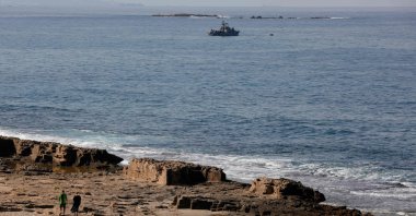 People walk along the beach as an Israeli Navy vessel patrols the Mediterranean waters off Rosh Hanikra, known in Lebanon as Ras al-Naqura, in the border area between the two countries, Oct. 7, 2022. (AFP Photo)