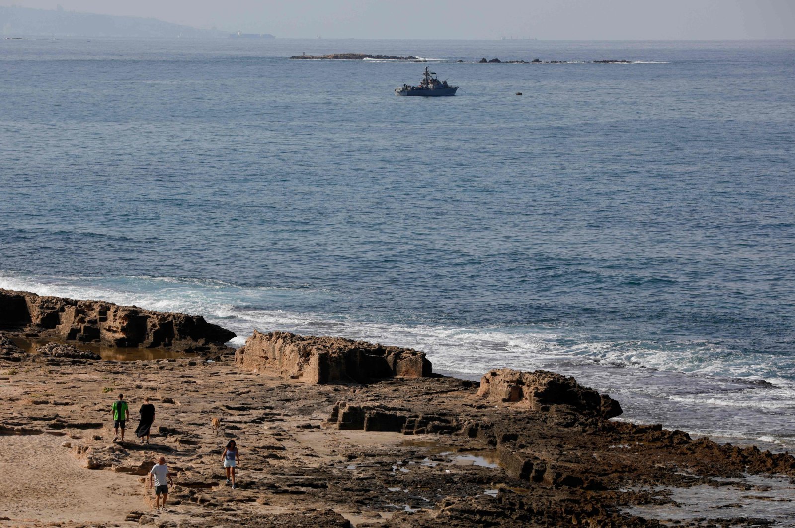 People walk along the beach as an Israeli Navy vessel patrols the Mediterranean waters off Rosh Hanikra, known in Lebanon as Ras al-Naqura, in the border area between the two countries, Oct. 7, 2022. (AFP Photo)