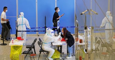 Medical workers in protective suits gather swabs from passengers for nucleic acid testing, at an arrival hall of Shanghai Hongqiao International Airport, China, Oct.12, 2022. (REUTERS Photo)