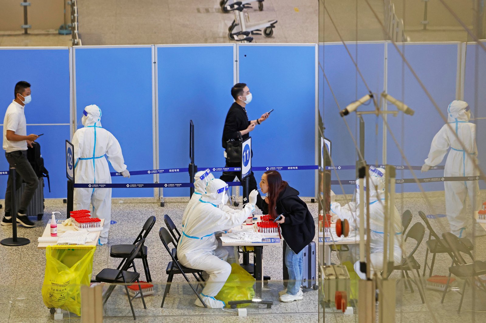 Medical workers in protective suits gather swabs from passengers for nucleic acid testing, at an arrival hall of Shanghai Hongqiao International Airport, China, Oct.12, 2022. (REUTERS Photo)