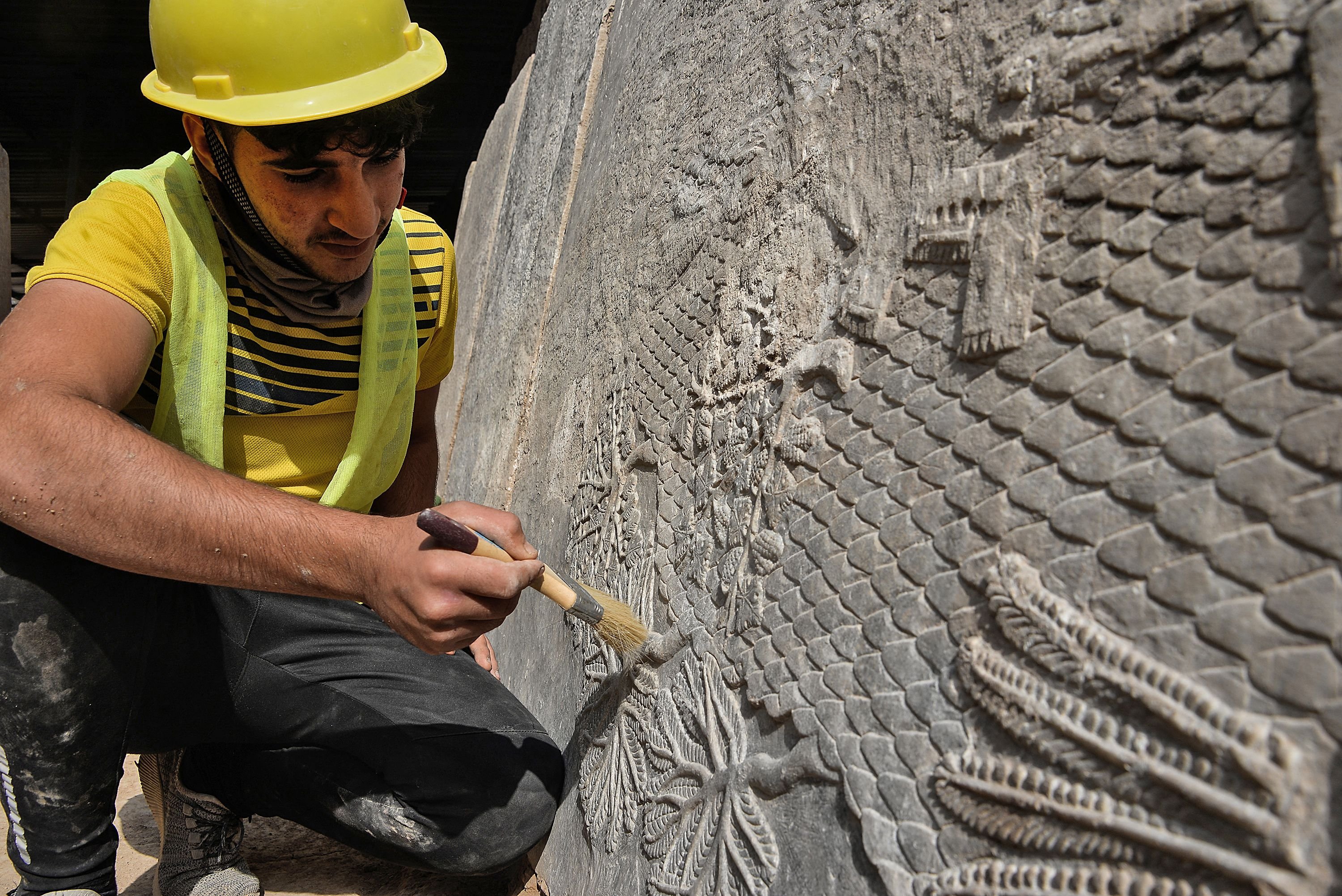 Seorang pekerja Irak menggali relief pahatan batu yang baru-baru ini ditemukan di Gerbang Mashki, salah satu gerbang monumental ke kota kuno Niniwe, Asyur, di pinggiran kota Mosul, Irak utara, 19 Oktober 2022. (AFP Photo)