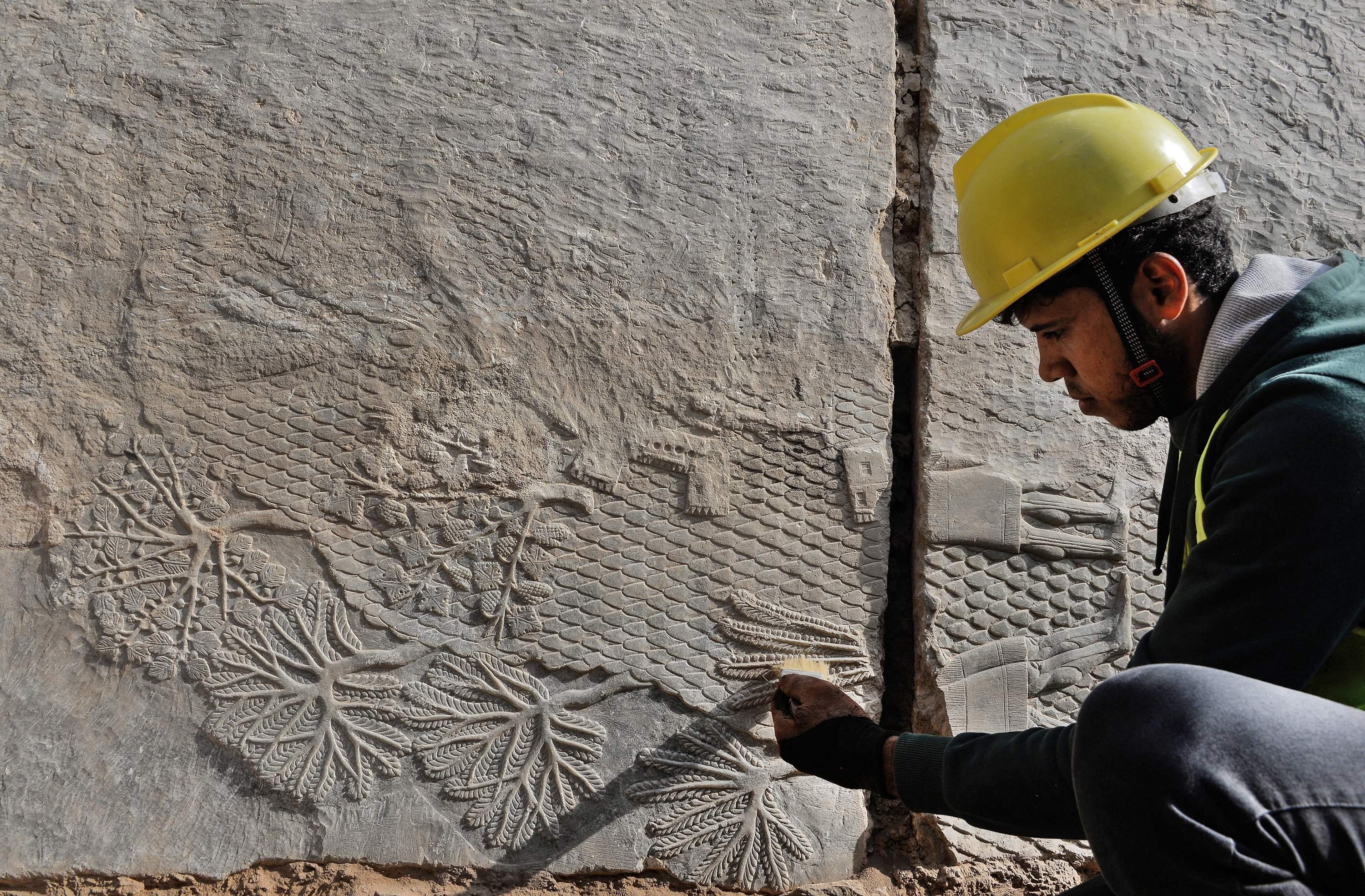 Seorang pekerja Irak menggali relief pahatan batu yang baru-baru ini ditemukan di Gerbang Mashki, salah satu gerbang monumental ke kota kuno Niniwe di Asyur, di pinggiran kota Mosul, Irak utara, pada 19 Oktober 2022. (AFP Photo)